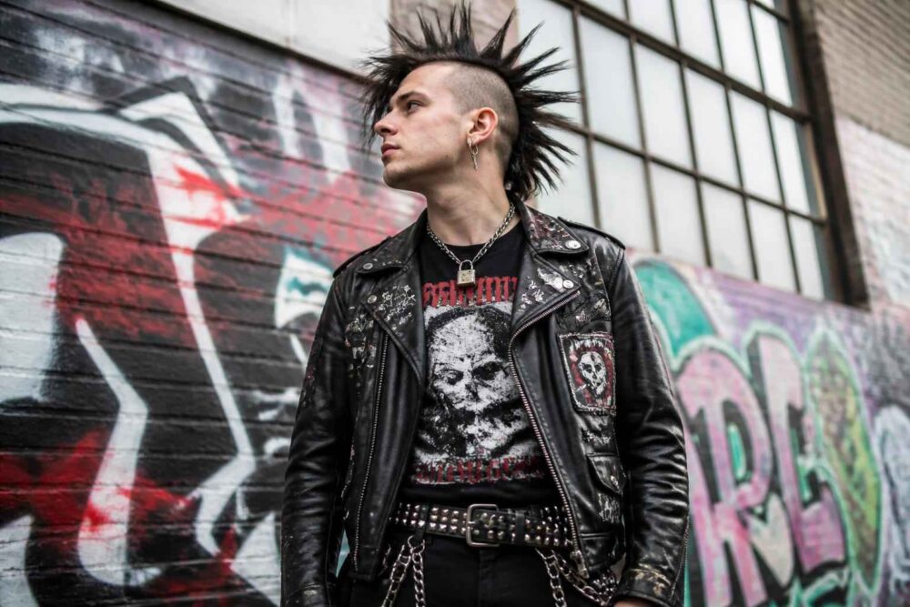 Punkowiec w czarnej skórzanej kurtce stoi przed ścianą pokrytą graffiti